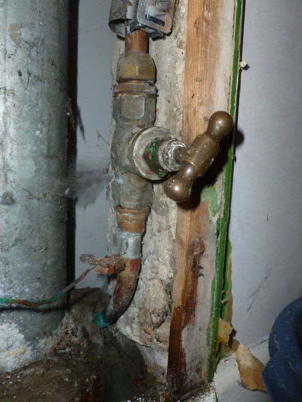 Corroded stopcock on a pipe inside a wall