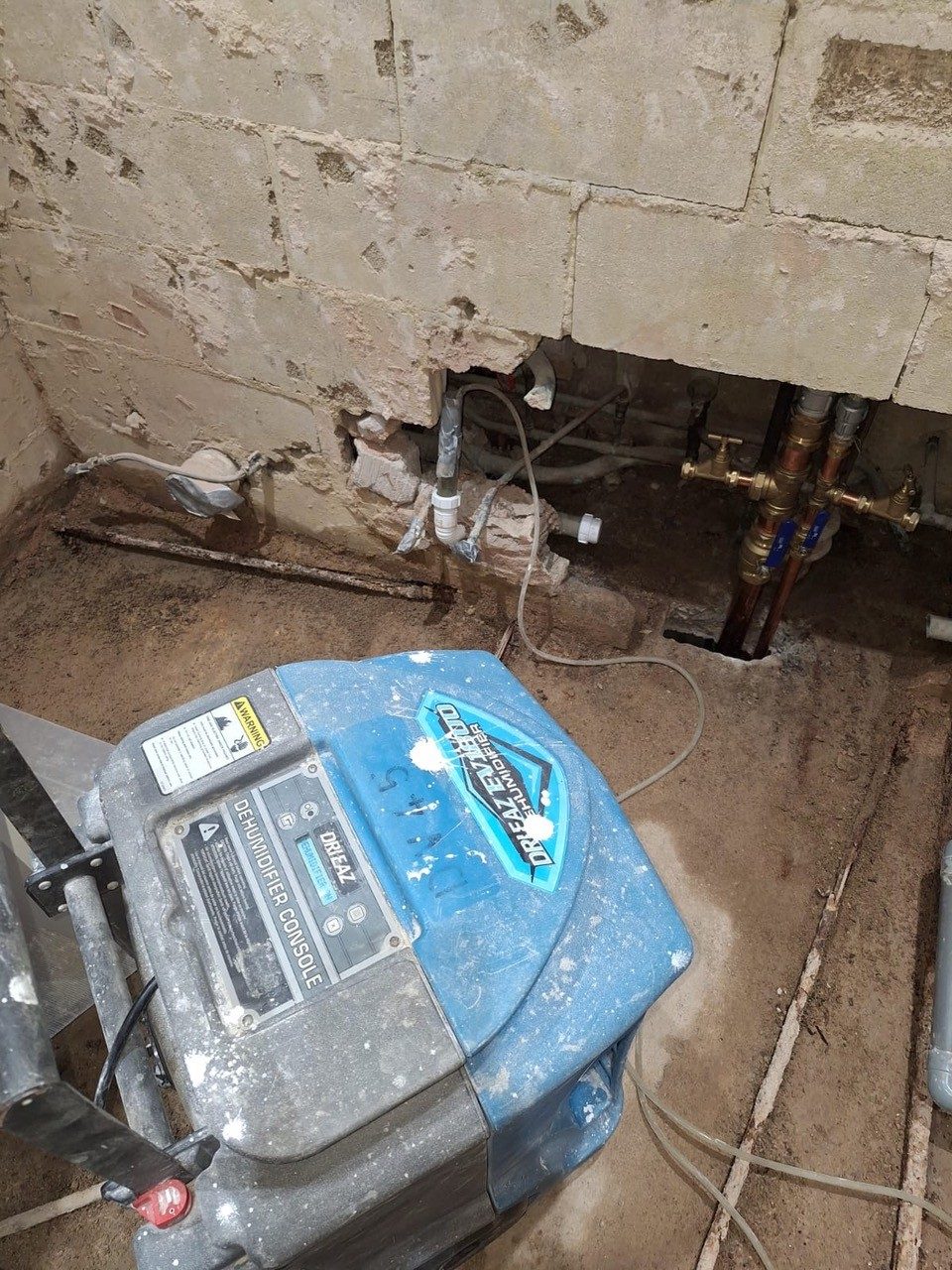Dehumidifier drying out an opened-up floor beside exposed pipework