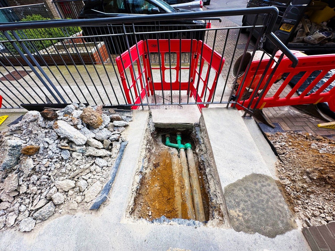 Trench dug to reach a leaking water main, behind safety barriers