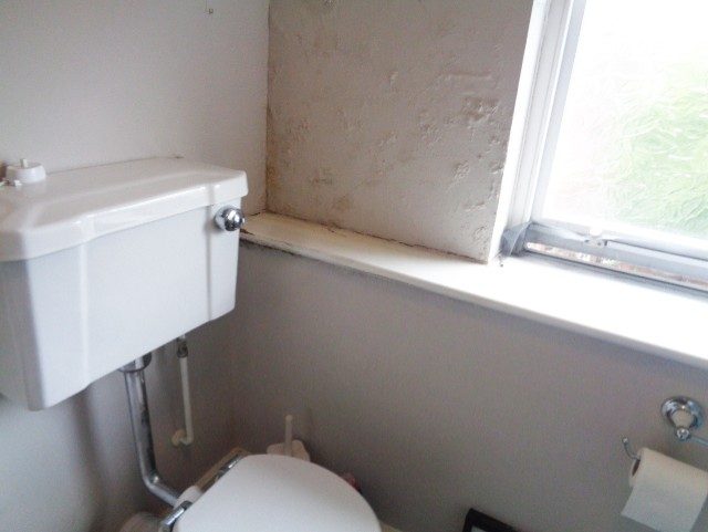 Damp staining on a wall beside a toilet window
